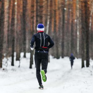 male athlete runner running in falling snow in forest in marathon winter
